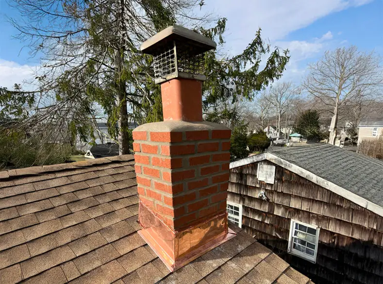 A brick chimney with freshly installed copper base on top of a two story shingle roof.
