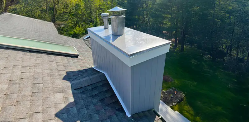 Metal and wood chimney atop a two-story roof with skylight.